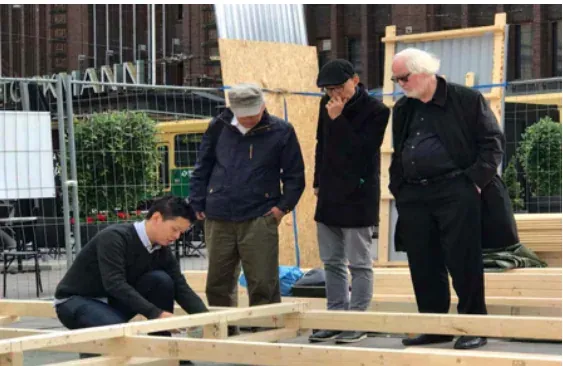 A volunteer kneeling at the timber frame while three people watch.