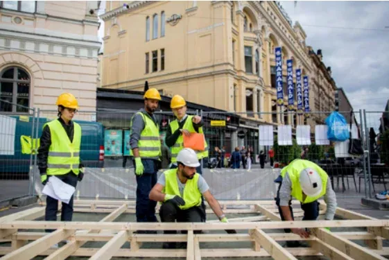 Volunteers in hard hats and hi-vis vests laying out the timber floor frame in the square.