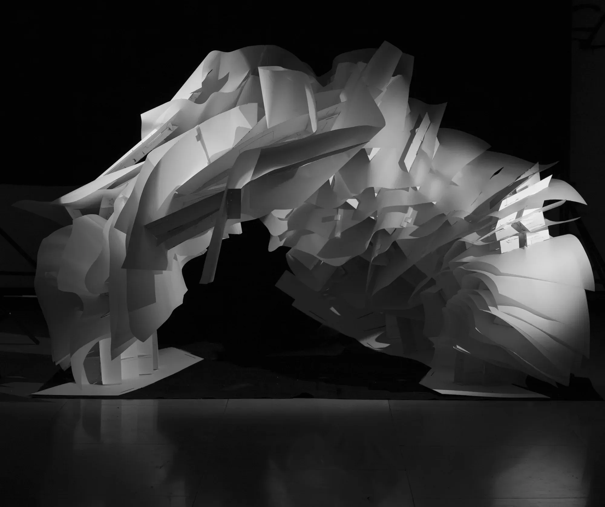 A cave-like structure of hundreds of curved white paper sheets, lit from inside against a black background.