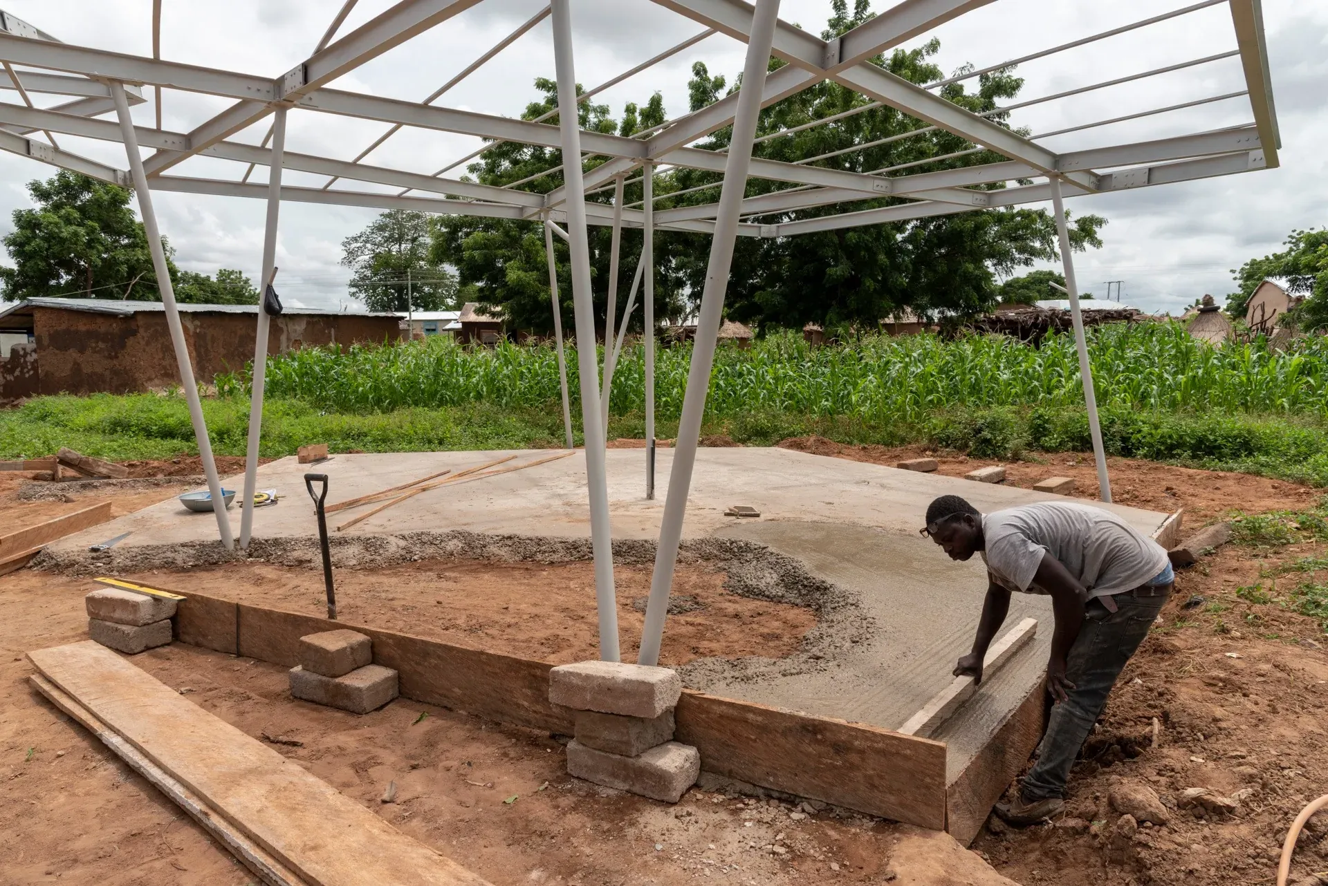 A builder laying blocks around the base of a column under the steel roof frame.