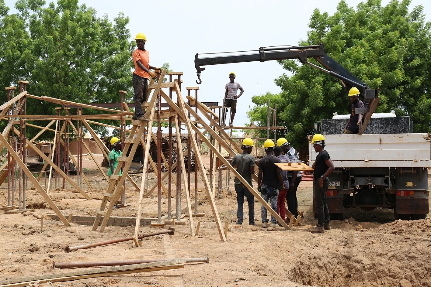 Workers in hard hats lifting a timber-braced roof element with a truck-mounted crane.