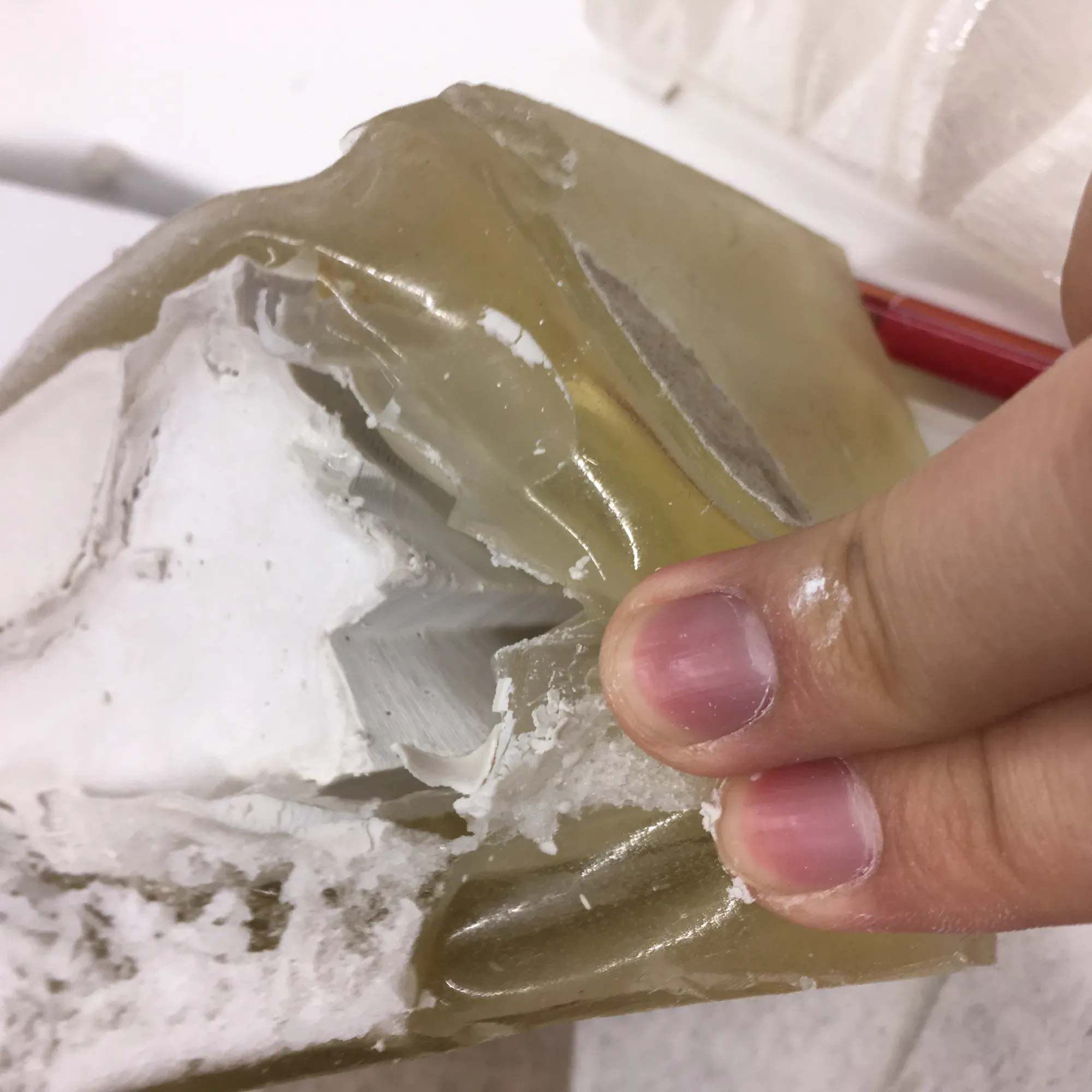 Hands holding a translucent amber gelatin mould with a white plaster cast inside.