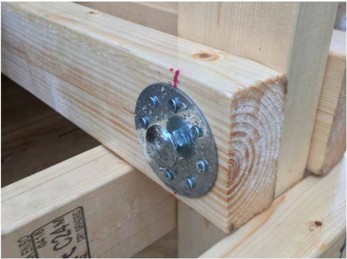 Close-up of a timber joint: two beams joined with a round metal plate and bolt.