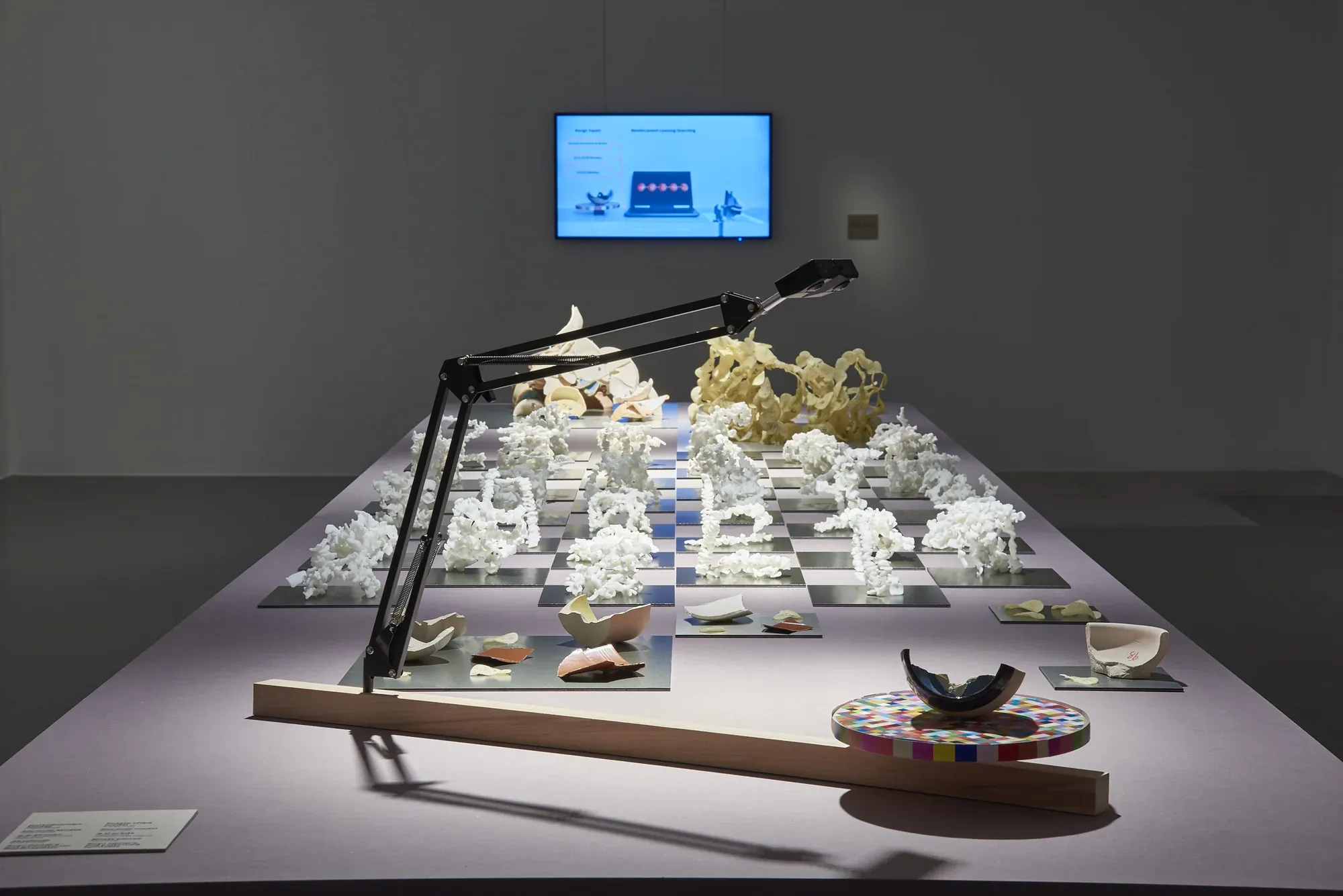 A long table of small white shell models; in front, a scanner arm and a fragment on a turntable.