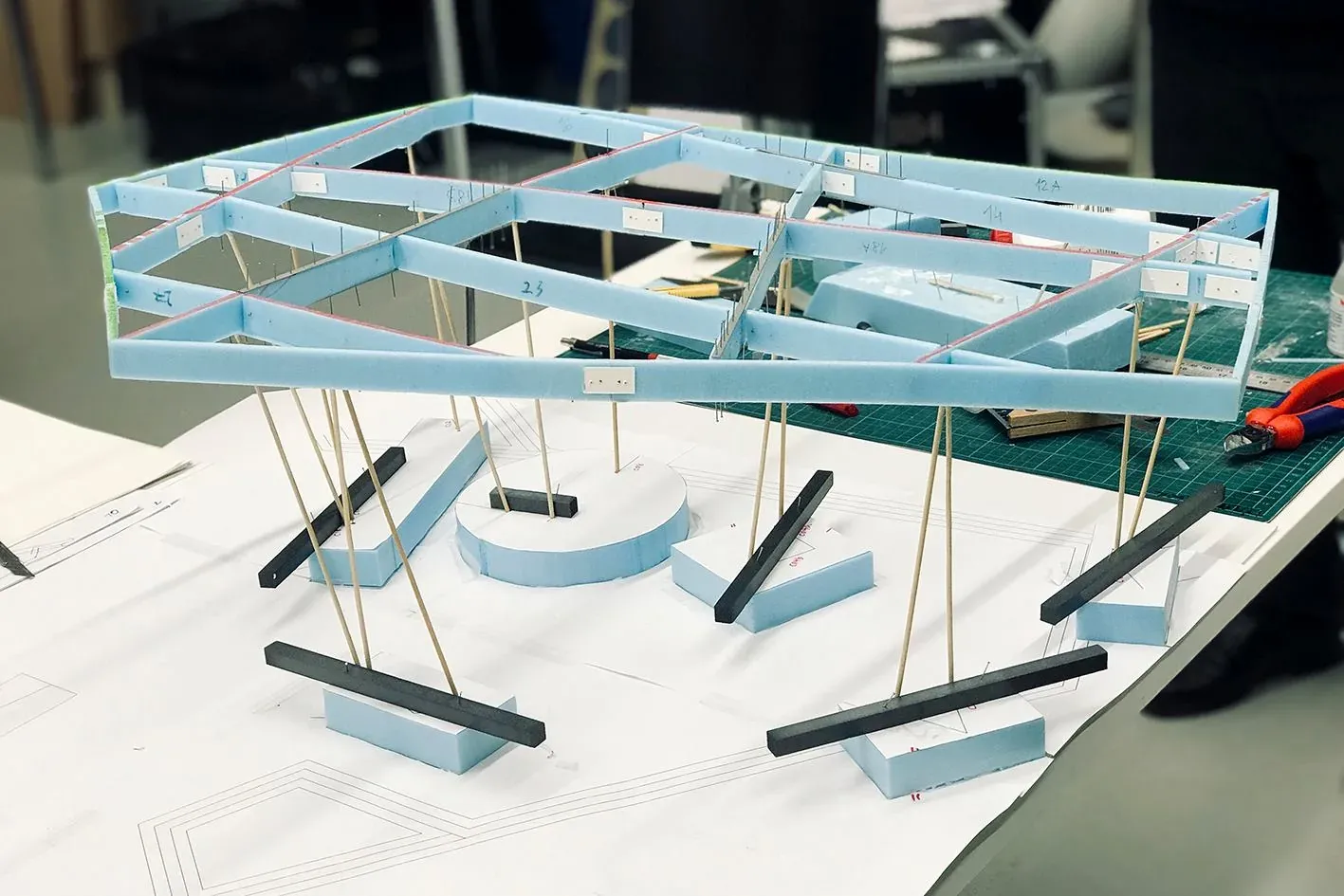 A physical model of the steel roof structure: light-blue frames on thin dark columns.
