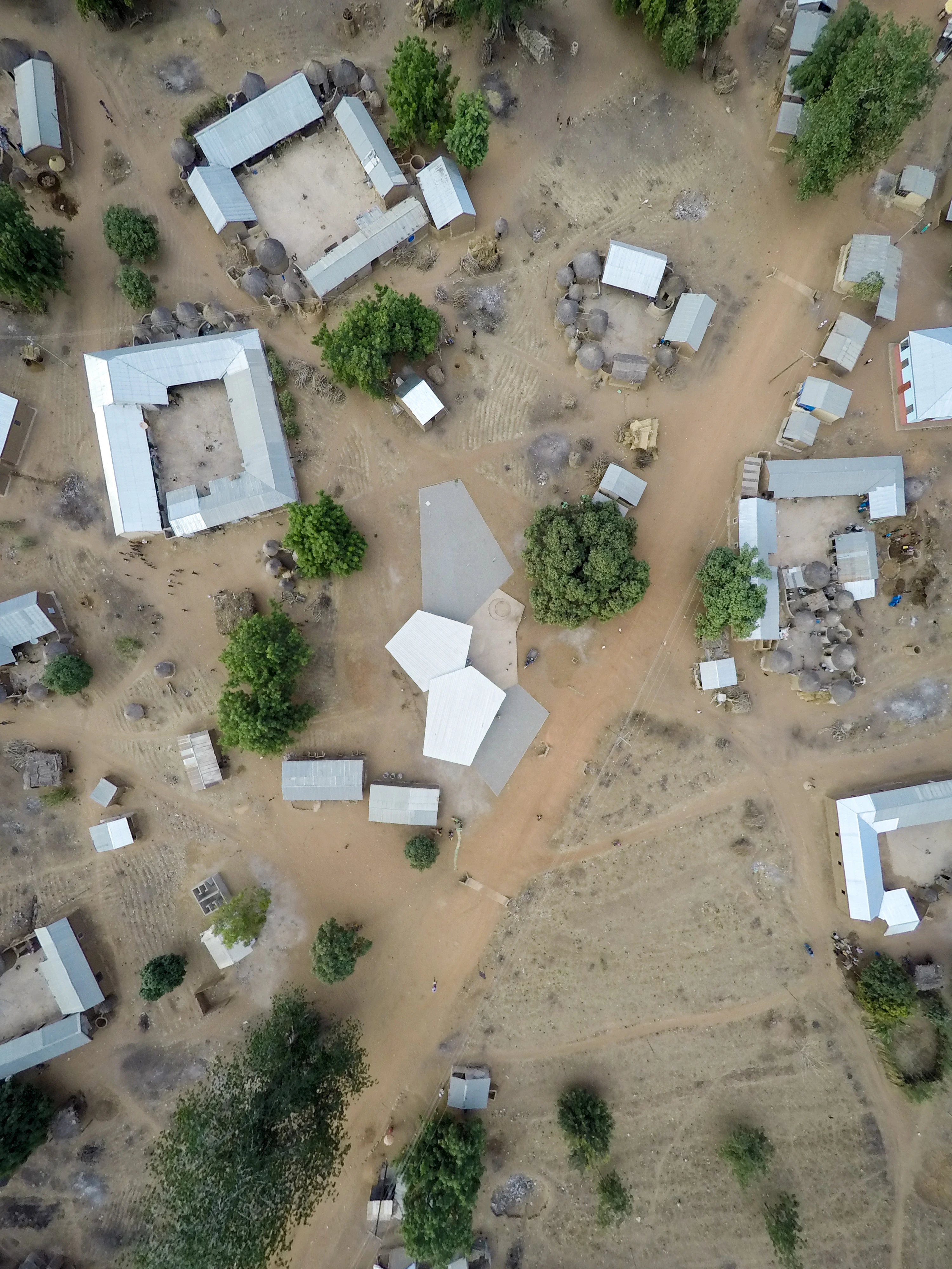 Drone photograph looking straight down on the market’s roofs among houses, trees and dirt paths.