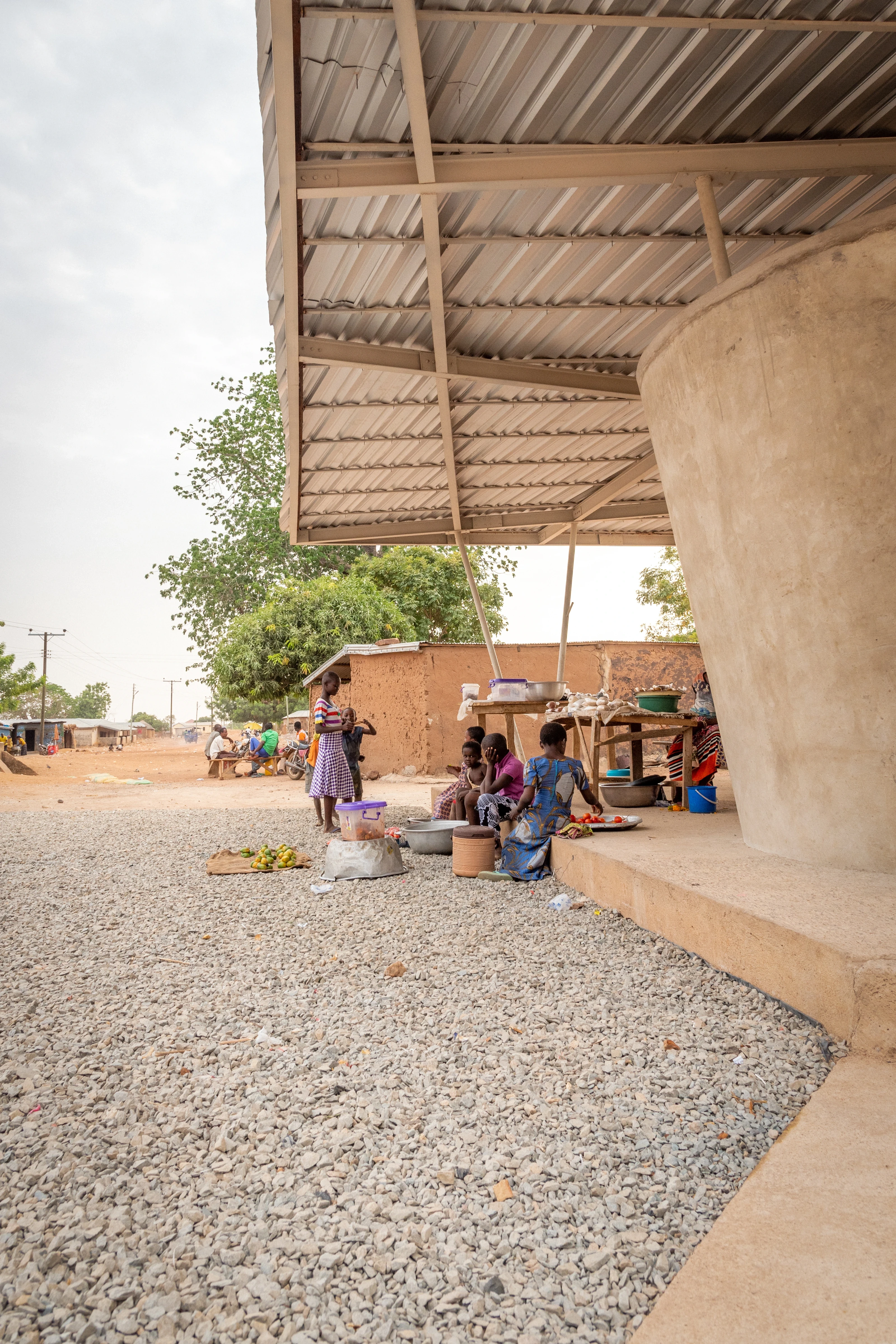 Looking along the market’s gravel floor under the corrugated roof, a concrete column on the right and traders behind.
